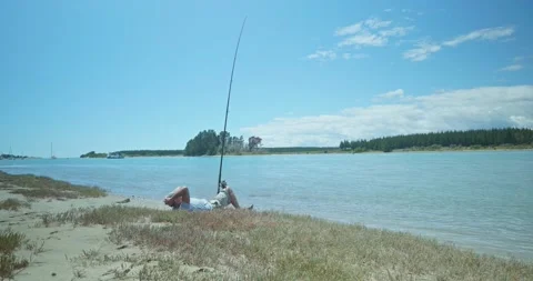 Man Lying Down Fishing on Beach, Sunny Calm Blue Waters, Surfcasting, 4K Stock Footage 239138313