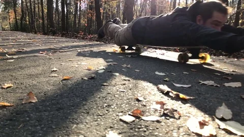 Man lying down on longboard and ride on the leafs covered path. Video stock 82524444