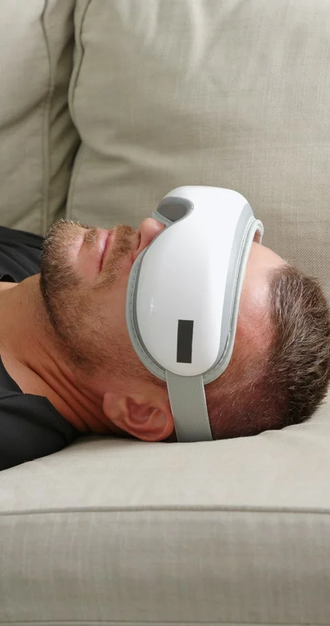 Man lying down on sofa with electric eye massager. Stock Footage 247159349