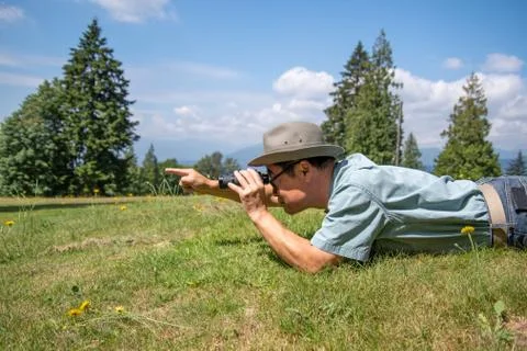 A  man lying down who using a pair of binoculars and pointing at something. Stock Photos