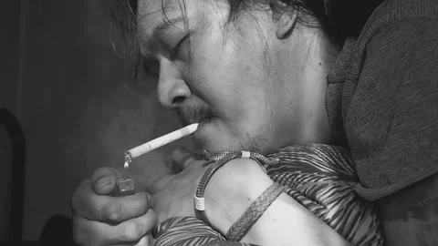 Man Lying Face Down Smoking a Cigarette in a Dimly Lit Room Stock Footage 333530178