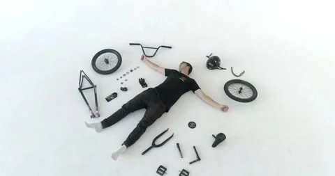 Man is lying on the floor next to the spare parts for bicycle and waving his 스톡 동영상 103247267