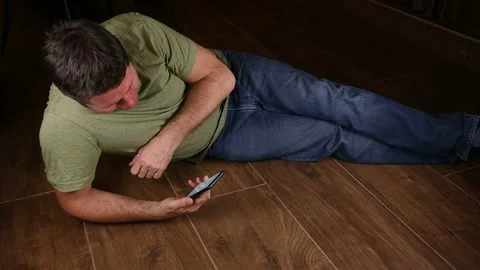 Man lying on the floor while enjoying watching something on his phone Stock Footage 229897015