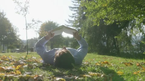 Man Lying on Grass, Absorbed in a Book Amidst Autumn Peaceful Beauty Stock Footage 300250944