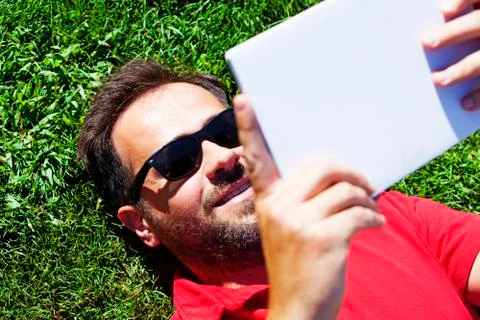 Man lying on the grass, enjoying a tablet. Stock Photos