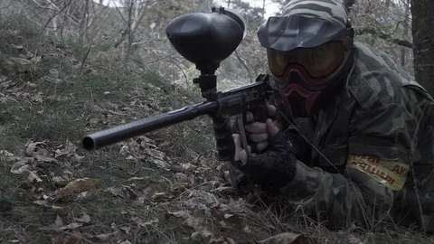A man lying on the grass shooting from a paintball in slow motion Stock Footage 83087469