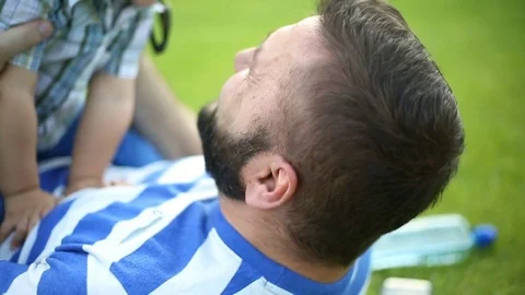 Man lying with his son on the grass in the park and having fun Stock Footage 76980824