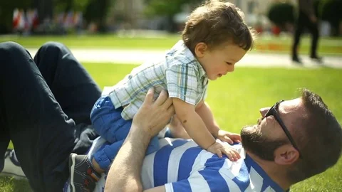 Man lying with his son on the grass in the park and relaxing Stock Footage 76981047