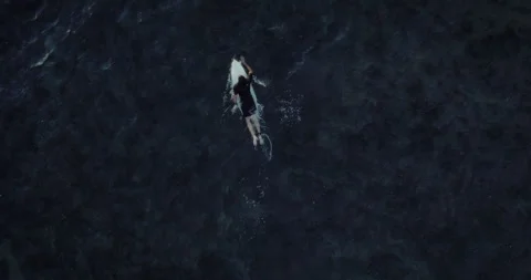 Man lying on his surfboard and paddling out into the ocean aerial Stock Footage 275577847