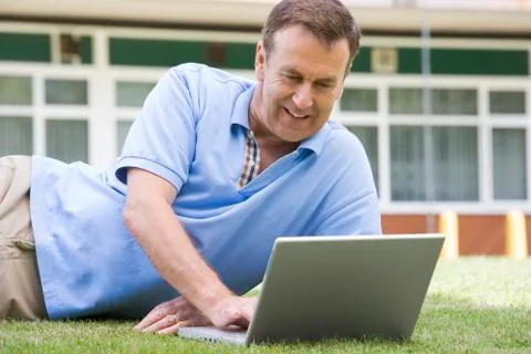 Man lying on lawn of school using laptop Stock Photos