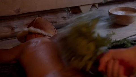 Man lying on plank bench receives relaxing back massage with oak brooms in Stock Footage 221940066