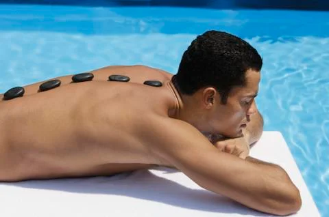 Man lying by pool, lava rocks on back Stock Photos