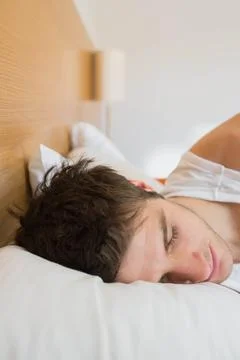 Man lying right side on bed, wearing white tank top, resting head on pillow near Stock Photos
