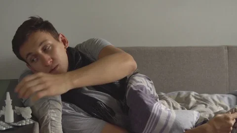 Man lying sick in bed next to his medications in his home and sprinkles a nasal Vídeo Stock 80673530