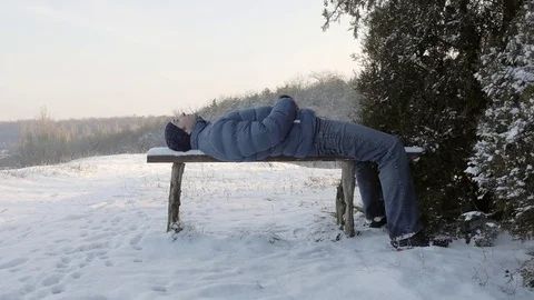 A man, lying on a snow-covered bench and enjoying the beautiful winter landscape Stock Footage 77208387