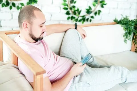 The man is lying on the sofa and looking at the phone screen Stock Photos