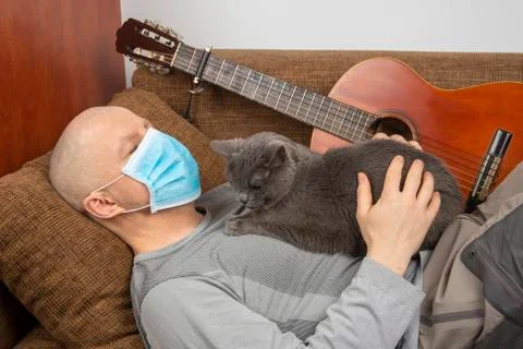 Man lying on a sofa with a gray cat during quarantine of coronavirus infectio Stock Photos