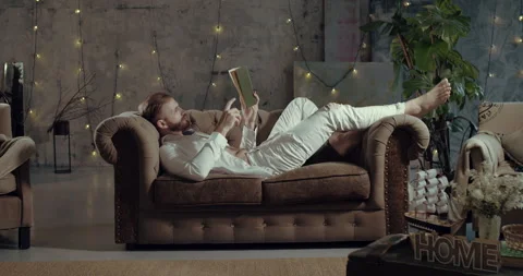 A man is lying on a sofa in the house and reading a book. Stock Footage 143791930