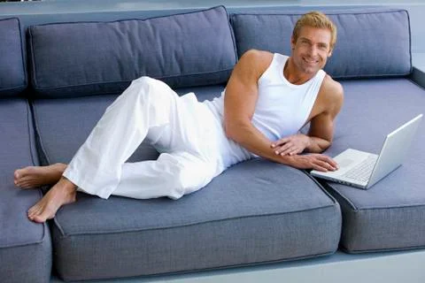 Man lying on sofa with laptop Stock Photos