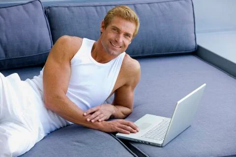 Man lying on sofa with laptop Stock Photos