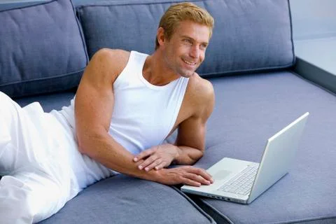 Man lying on sofa with laptop Stock Photos