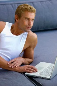 Man lying on sofa with laptop Stock Photos
