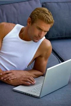Man lying on sofa with laptop Stock Photos