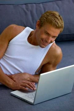 Man lying on sofa with laptop Stock Photos