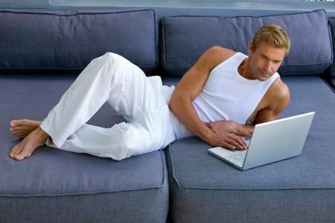 Man lying on sofa with laptop Foto stock