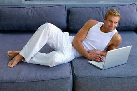 Man lying on sofa with laptop Stock Photos