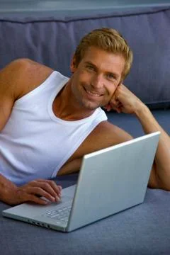 Man lying on sofa with laptop Stock Photos