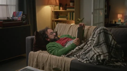 Man Lying on Sofa Looking at Digital Tablet in Cozy Living Room Stock Footage 341678973