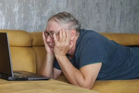 Man lying on sofa looking at laptop screen closely Stockfoto's