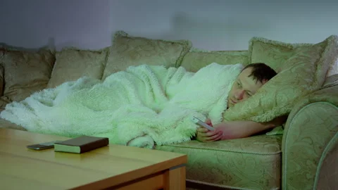 A man lying on the sofa at night in front of the TV with the remote control Stock Footage 306876124