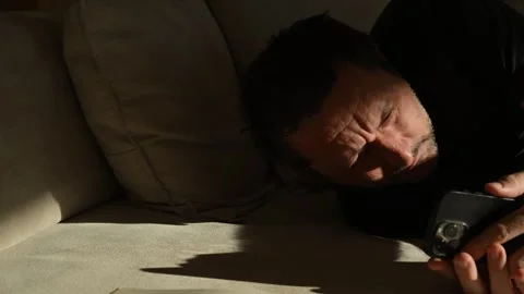 Man lying on sofa, staring blankly at smartphone, concept for depression an.. Stock Footage 329298265