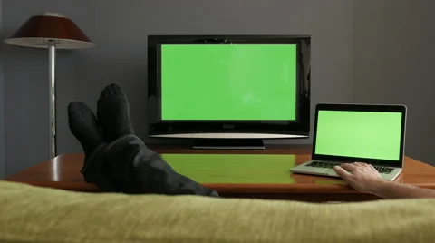Man lying on sofa, watching tv and clicking on laptop. Green screen. Stock Footage 54028094