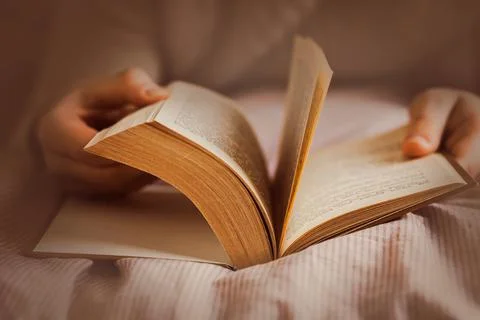 A man lying on a soft bed with a striped blanket is leafing through a thick o Stock Photos