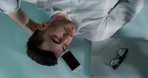 Man lying on the table with laptop, smartphone and glasses. He closes his eyes Stock Footage 120512428