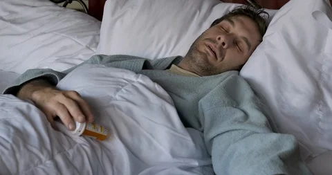 Man lying unconscious in bed dropping a pill bottle Stock Footage 108320038