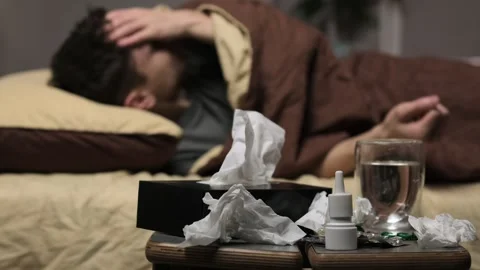 A man is lying very sick in bed, looking miserably ill. Medicines, water and Stock Footage 297479800