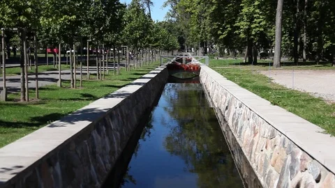 Man Made river with stone walls, bridge and red flowers Stock Footage 89662554