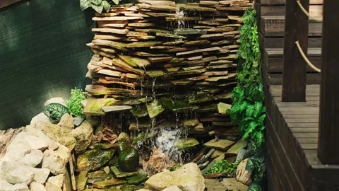 Man-made small waterfall with green plants around, water cascading over rocks in Stock Footage 284214450