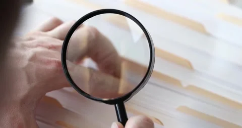 Man with a magnifying glass is sorting through folders with documents slow Stock Footage 257666678