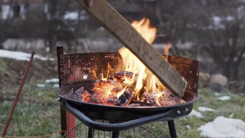 Man maintaining fire on a charcoal grill with a plastic plate and a wooden plank Stock Footage 100890094
