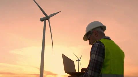 Man maintenance engineer works at wind farm at sunset with a laptop in his hands Stock Footage 255409343