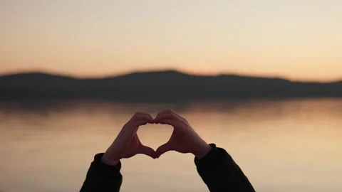 Man make Love heart shape from hands at sunset near by sea bay and mountains Stock Footage 229725449