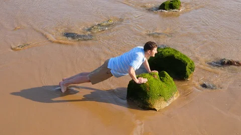 Man make push-up exercise at beach, put hands on green stone Stock Footage 128663920