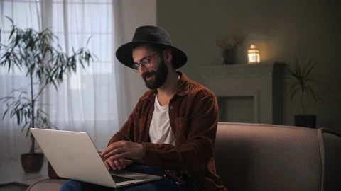 Man make video call sitting at couch in home interior using laptop.Young guy Stock Footage 212318032