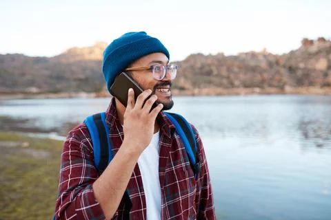 A man makes a call on smartphone while hiking in the mountains at a lakeside Stock Photos