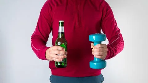 A man makes a choice between a bottle of beer and a workout with dumbbells - Stock Photos